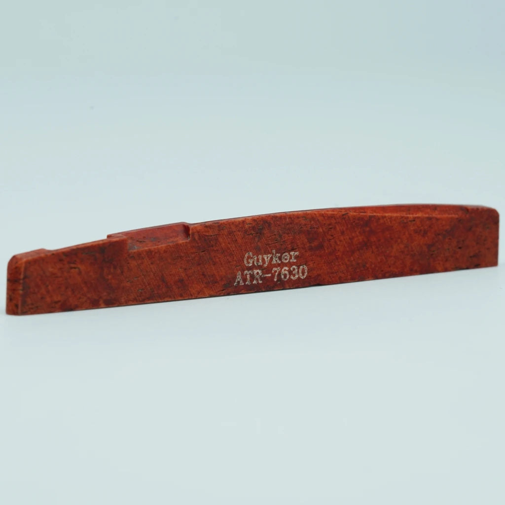 A wooden acoustic guitar bridge saddle with the inscription Guykər ATR-7630