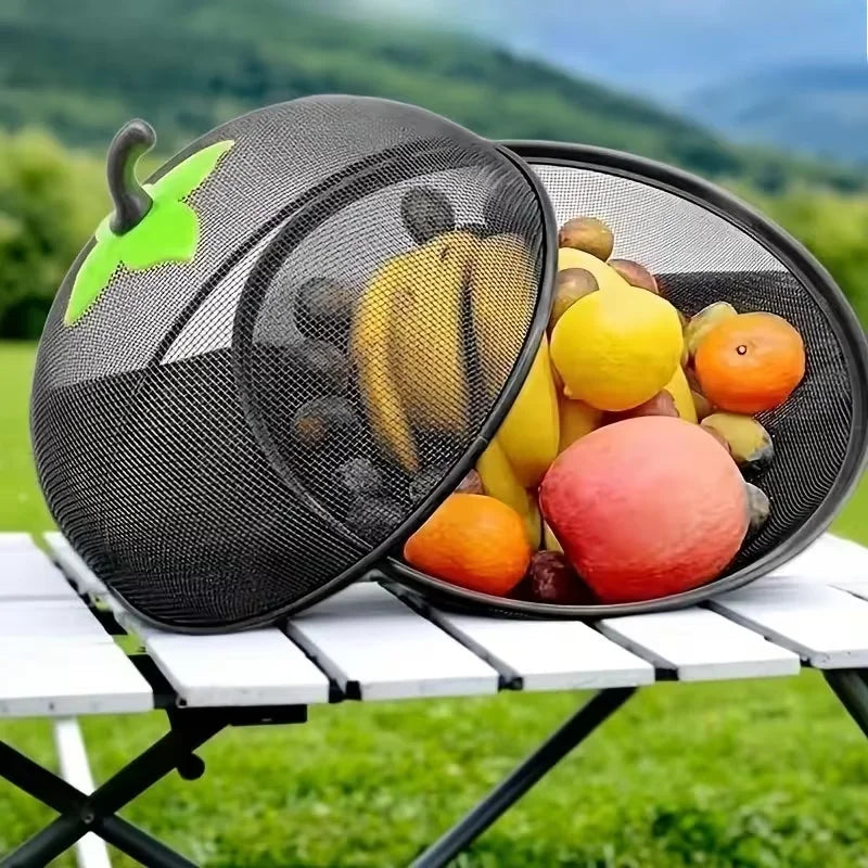 A black metal fruit basket with a mesh cover filled with various fruits outdoors.