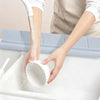 A hand is using a flexible silicone sink splash guard with a suction cup to clean a white sink.