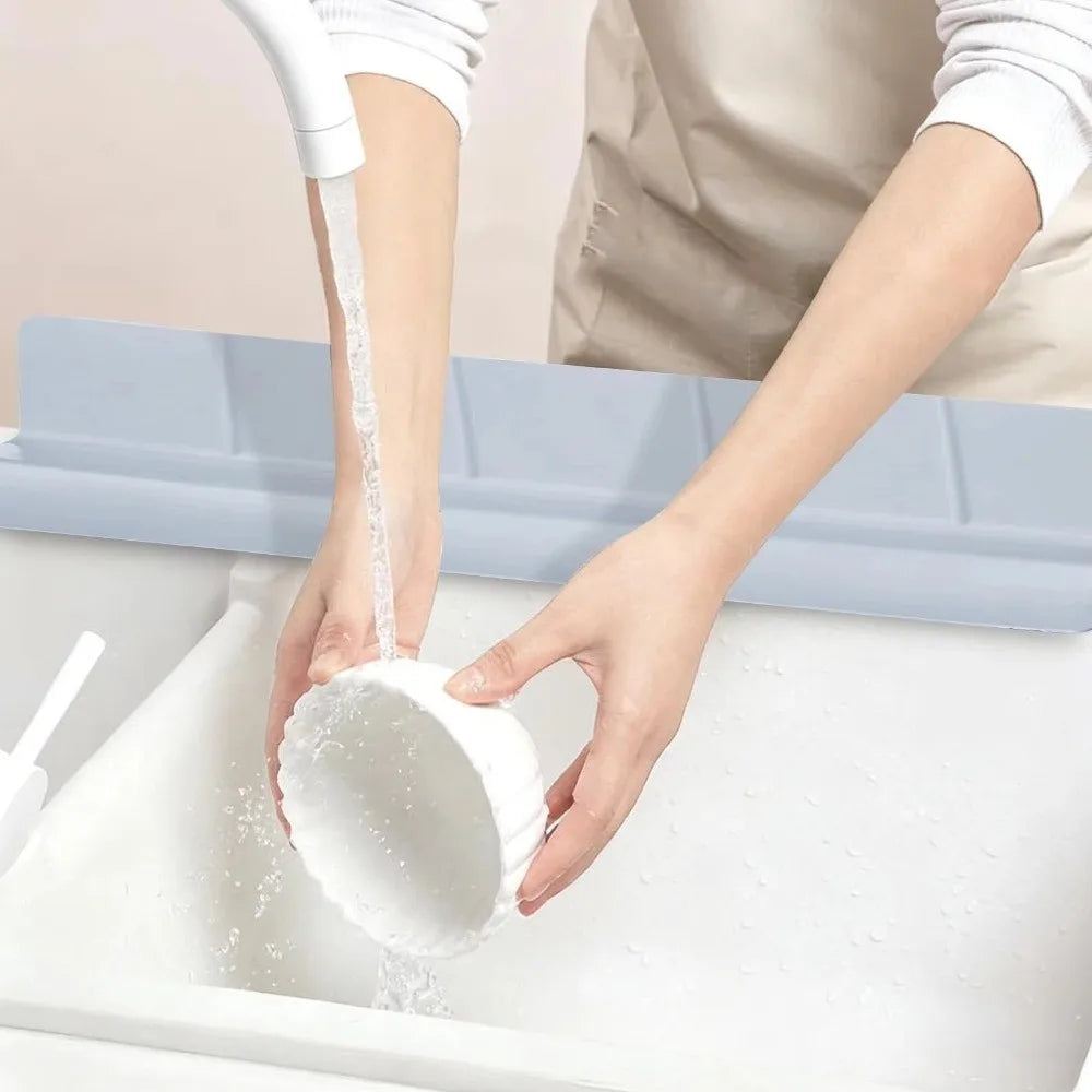 A hand is using a flexible silicone sink splash guard with a suction cup to clean a white sink.