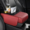 A red leather car armrest cushion with storage and cup holders is placed on a black car seat.
