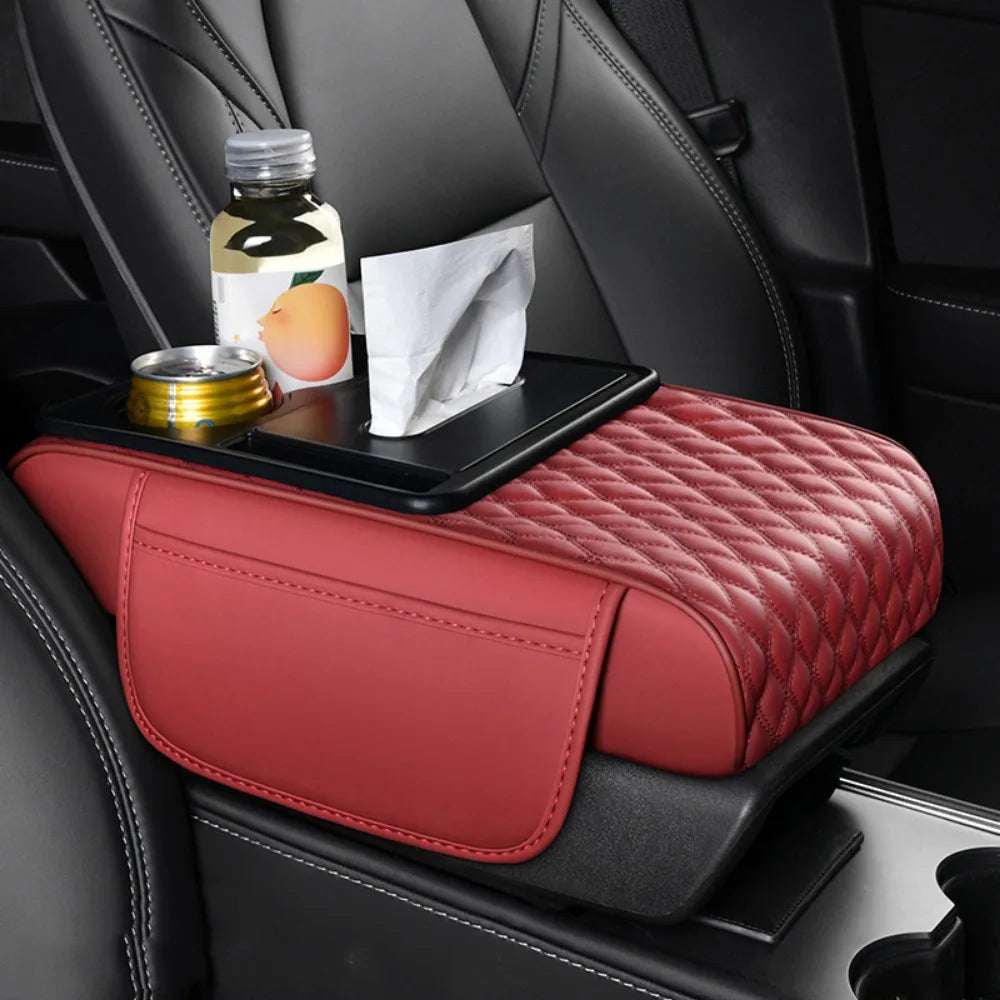 A red leather car armrest cushion with storage and cup holders is placed on a black car seat.