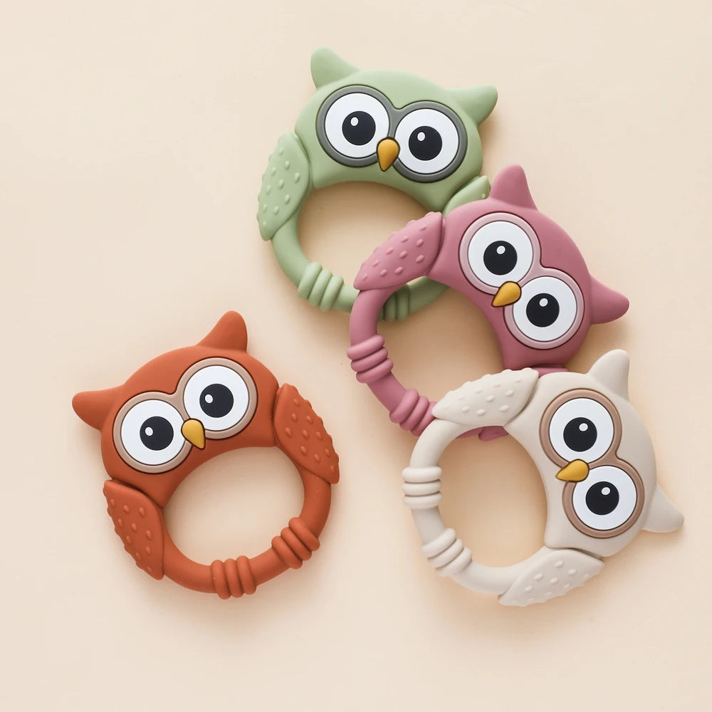 Three silicone owl-shaped teethers and rattles in green, pink, and beige tones