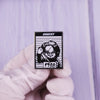 A hand wearing a white glove holds a black enamel pin featuring Chucky from the horror movie with the year 1988 engraved.