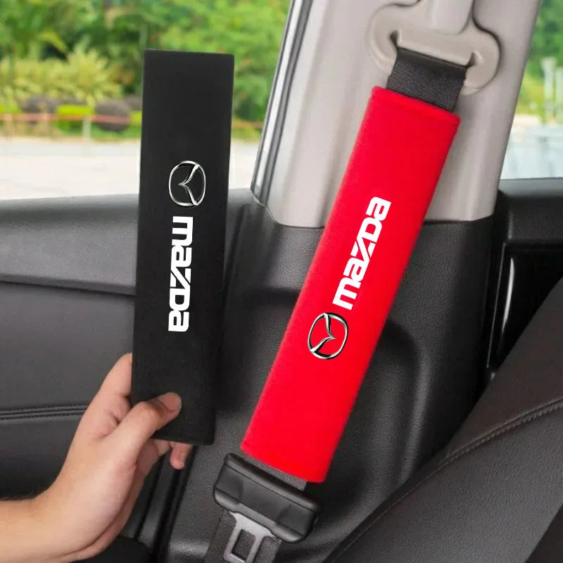 A red Mazda car seat belt shoulder protector cover is shown next to a black Mazda branded strap in a car interior.