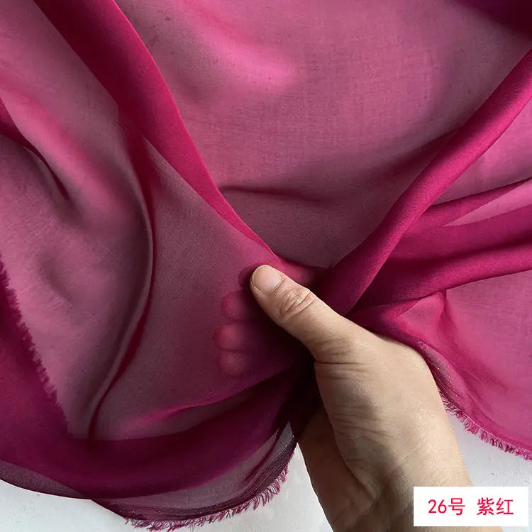 A hand is folding a piece of sheer magenta silk chiffon fabric.