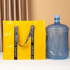 A yellow tote bag with black straps is displayed next to a blue plastic bottle.