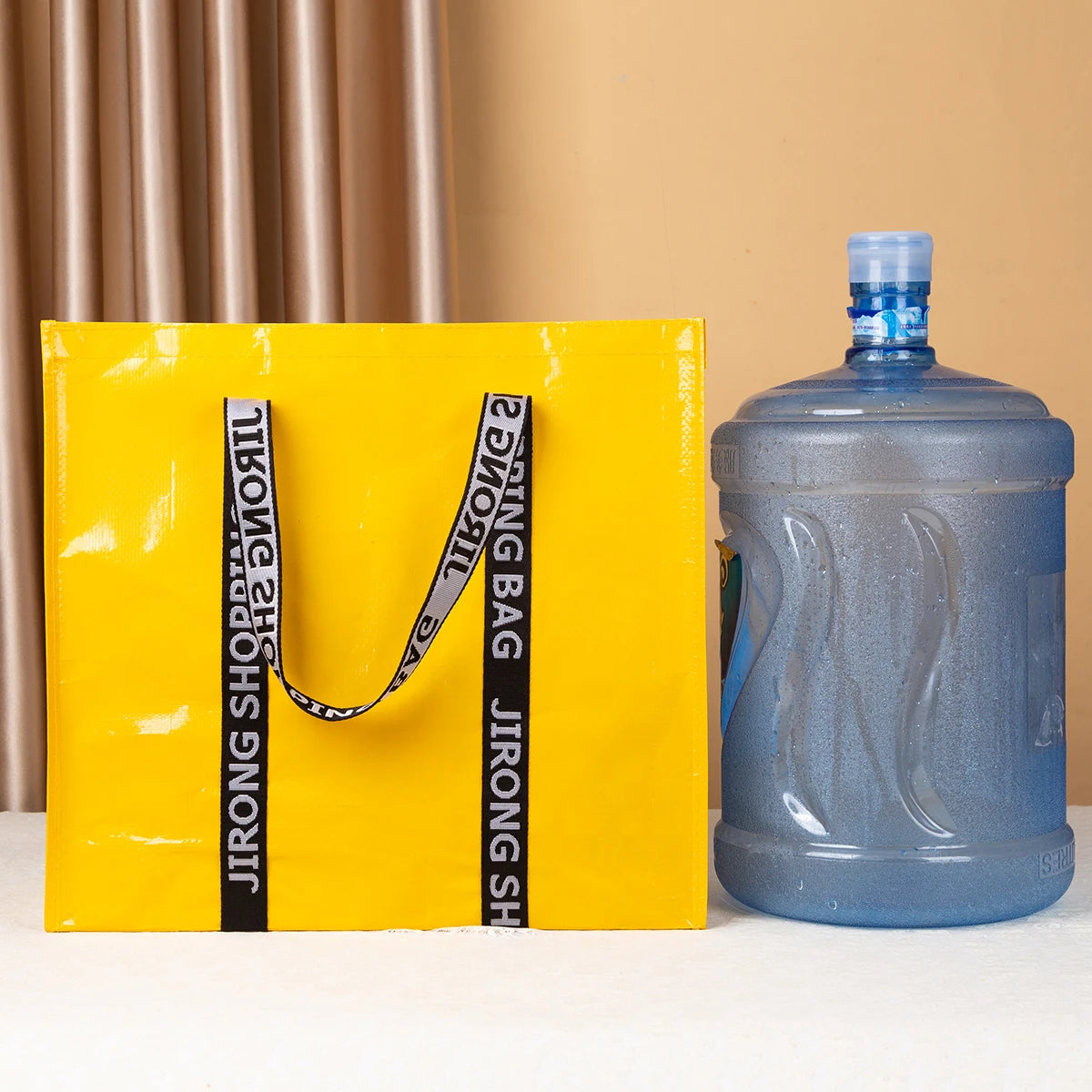 A yellow tote bag with black straps is displayed next to a blue plastic bottle.