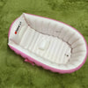 Pink inflatable bathtub for babies and toddlers with a hand pump resting on green fabric.