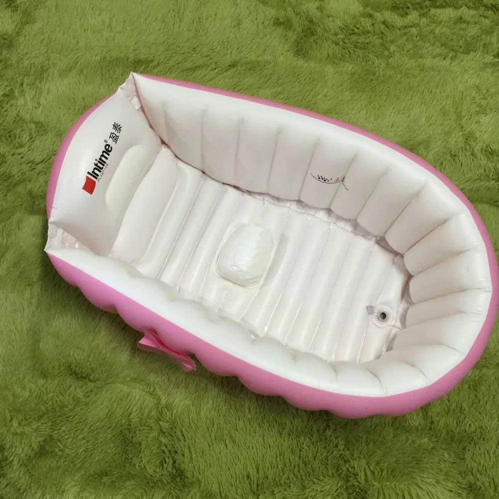 Pink inflatable bathtub for babies and toddlers with a hand pump resting on green fabric.