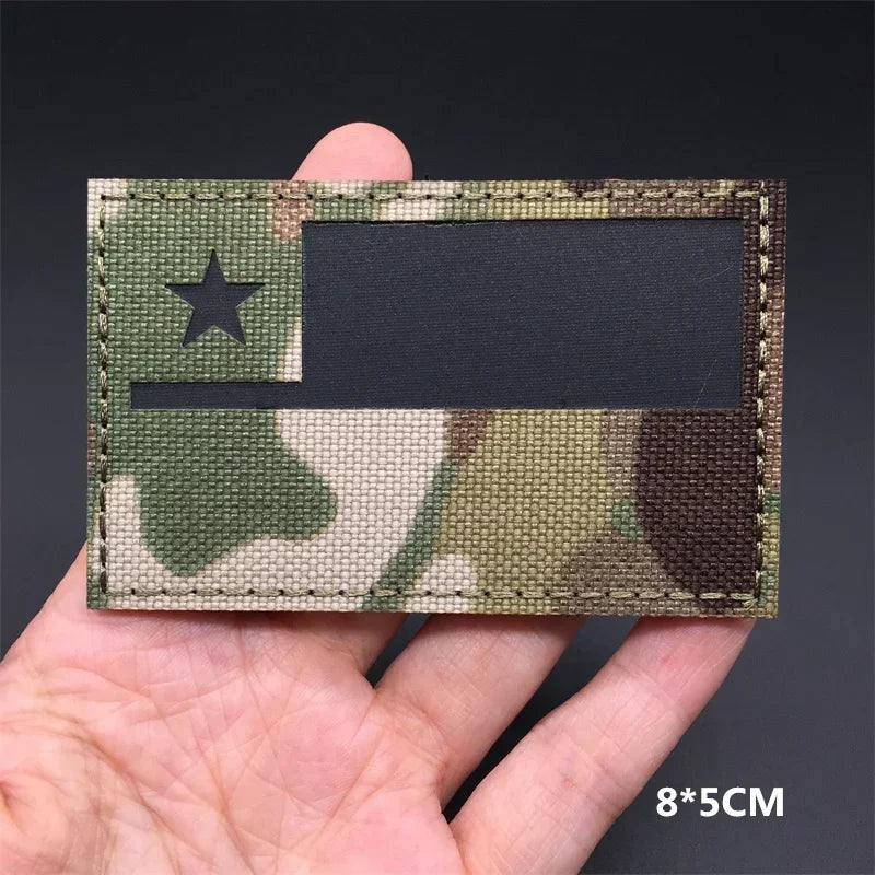 A rectangular tactical patch featuring a camouflage pattern with a black star and a dark rectangular insert on a hand.