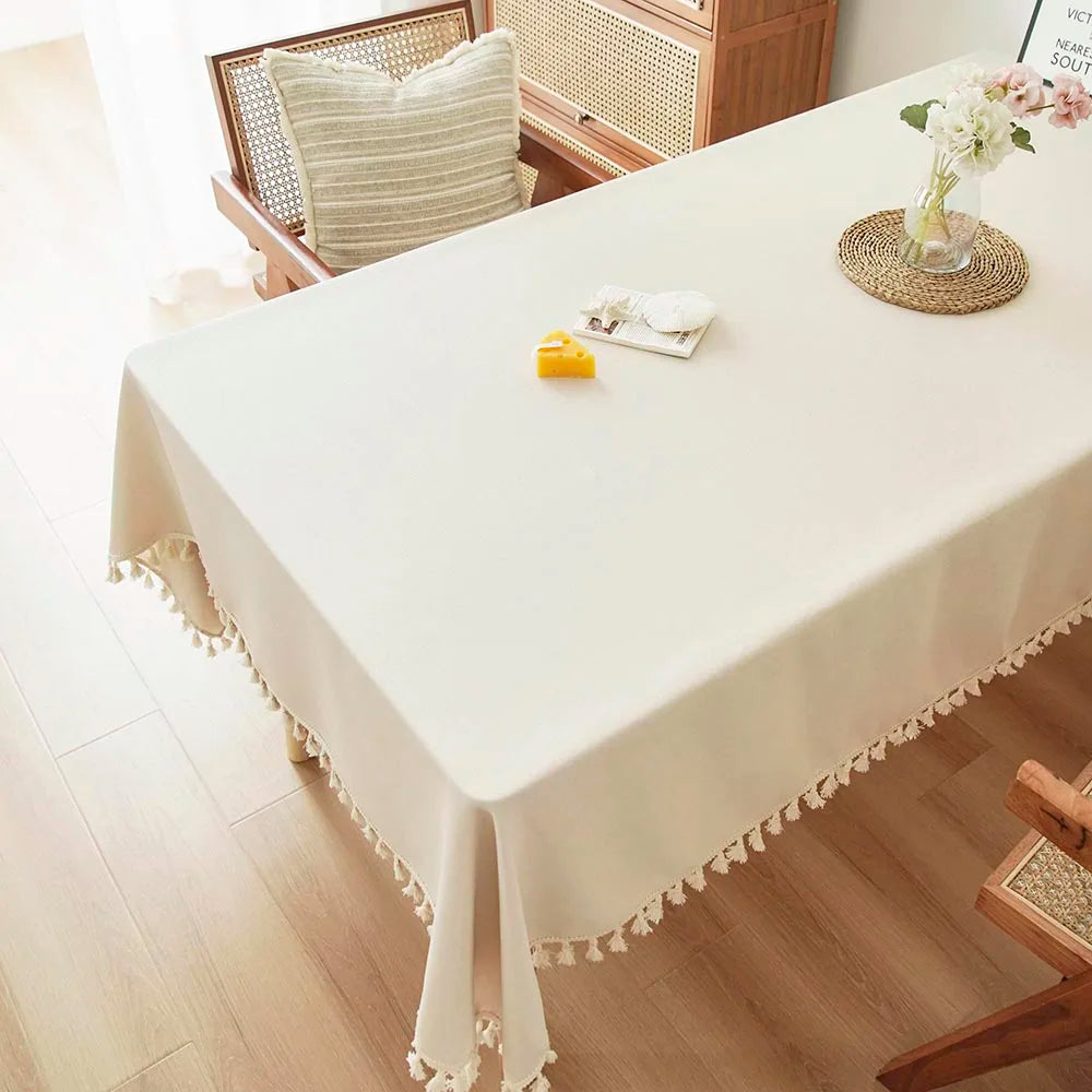 A white rectangle dining table covered with a cream tablecloth featuring delicate cotton tassels.