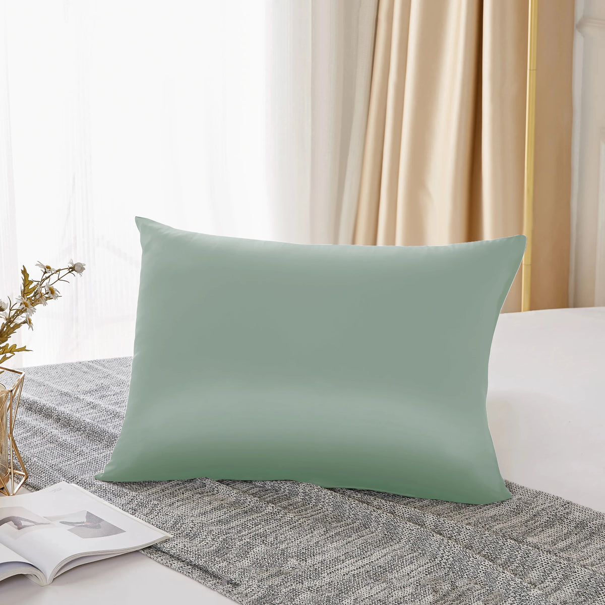 Housse de couette en soie mulberry vert sauge naturel posée sur un tissu gris texturé.