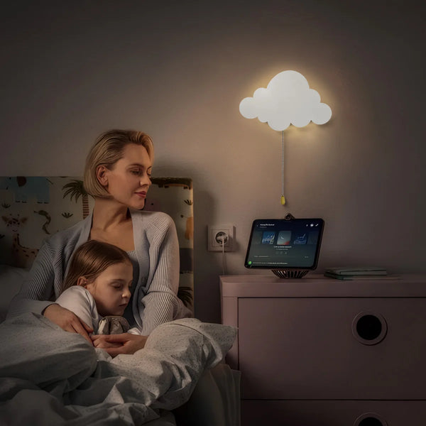 Una mujer está sentada con un niño en una guardería iluminada por una luz nocturna de nube flotante.