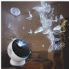 A white projector night light with a blue light beam is shown in a room decorated with moon and butterfly imagery.