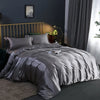 A luxurious gray silky duvet cover set displayed on a bed with a gold headboard and dark gray curtains.