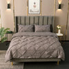 A gray 3D pinch pleated duvet cover set displayed on a bed with a padded headboard and modern lighting.