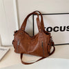 A brown vintage leather tote bag with multiple pockets resting on a white surface next to a framed object.