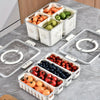 A white portable snack container with compartments holds various fresh fruits like apples, oranges, and berries.