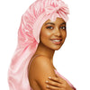 A woman wearing a pink satin sleep bonnet tied in a bow, shown from the side.