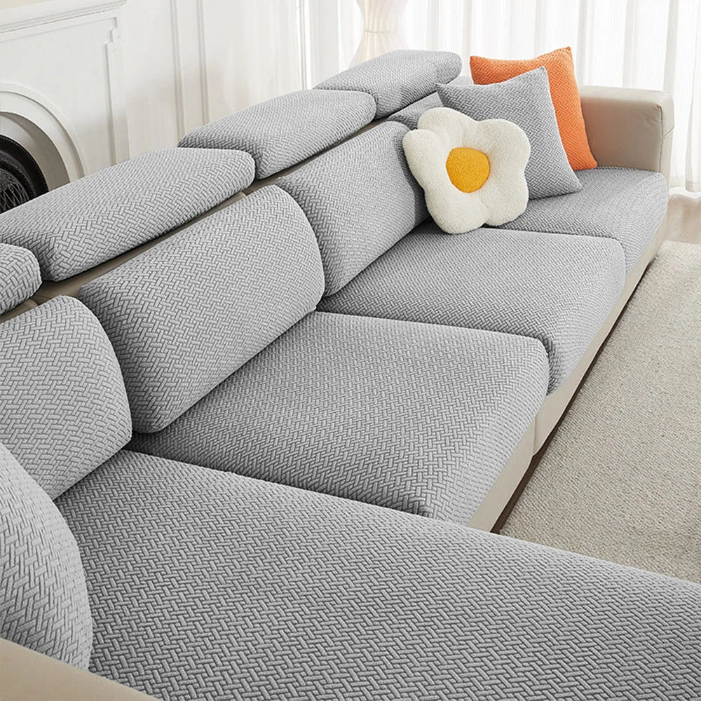 A gray jacquard elastic sofa slipcover with orange accent pillows on a light-colored sofa.