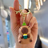 A hand holds a brown capybara keychain charm with a green accessory.