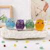 A collection of handcrafted crystal owl figurines in various colors resting on a natural crushed stone surface.