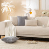 A beige sofa with gray and cream cushions, a white statue, and a white plant on a light rug.