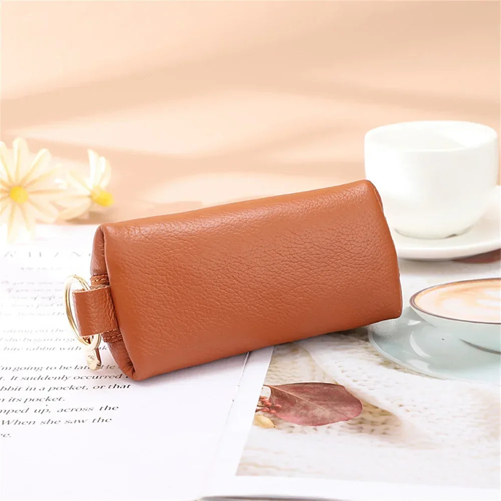 A brown PU leather key organizer wallet with a zipper lying on a white surface next to a cup of coffee.