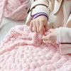 A person's hands are knitting a pink chunky chenille yarn, showing the texture and color of the fiber.