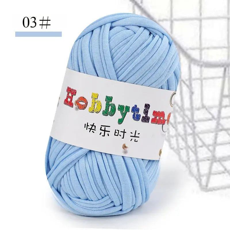 A ball of light blue soft T-shirt yarn for crochet and knitting is shown next to a wire basket.