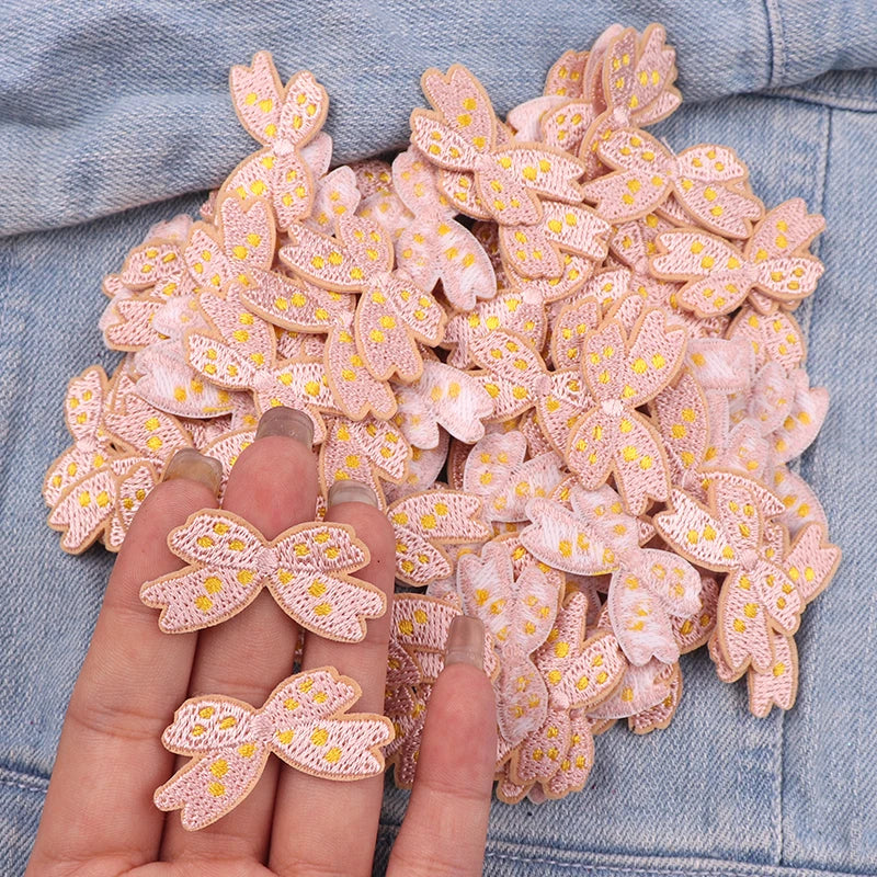 Pink embroidered iron-on patches shaped like cute cartoon bows on a denim fabric.