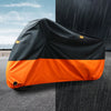 Housse de protection universelle orange et noire pour moto, posée sur l'asphalte sous la pluie et le soleil.
