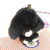 A black fluffy angel bunny keychain with a pom pom tail resting on a red and white striped surface.