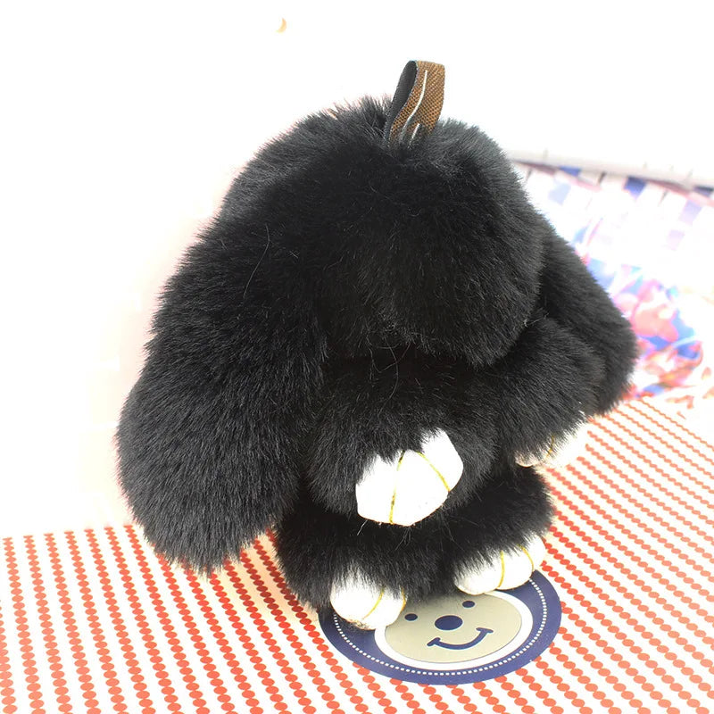 A black fluffy angel bunny keychain with a pom pom tail resting on a red and white striped surface.
