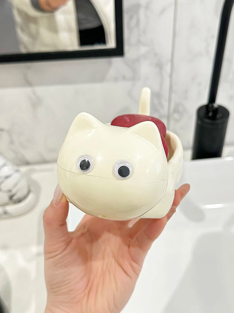 A hand holds a white cat-shaped soap box with a red drainage tray against a white tiled background.