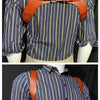 A man wearing a blue striped shirt with brown leather double shoulder suspenders.
