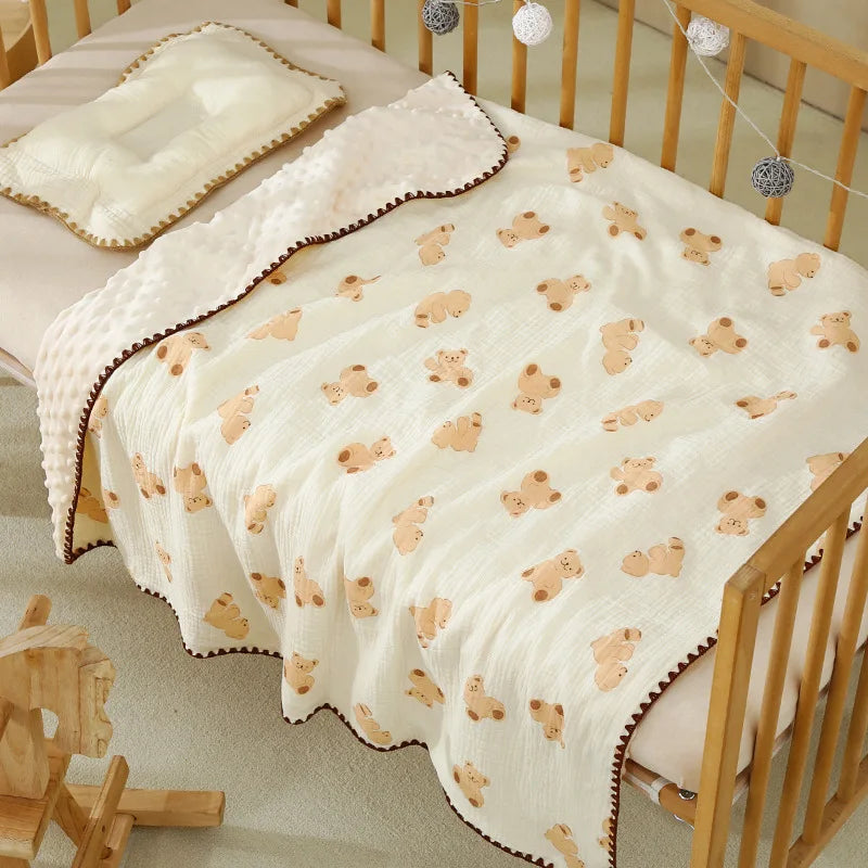 A white cotton gauze baby swaddle blanket with a bear print, draped over a wooden crib.