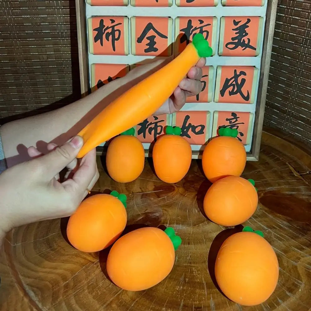 A hand holds an orange carrot-shaped squishy toy in front of a grid displaying Japanese characters.