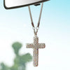 A silver stainless steel cross pendant adorned with rhinestones hanging from a chain, viewed against a blurred green backgrou