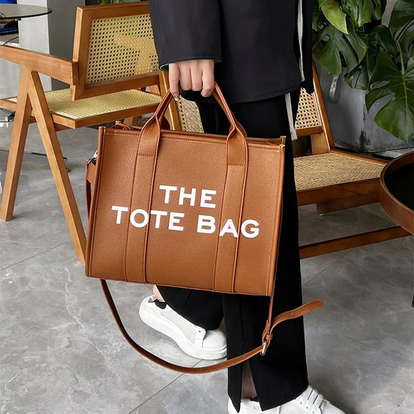 Una bolsa de cuero marrón con texto blanco es sostenida por una persona junto a sillas de madera.