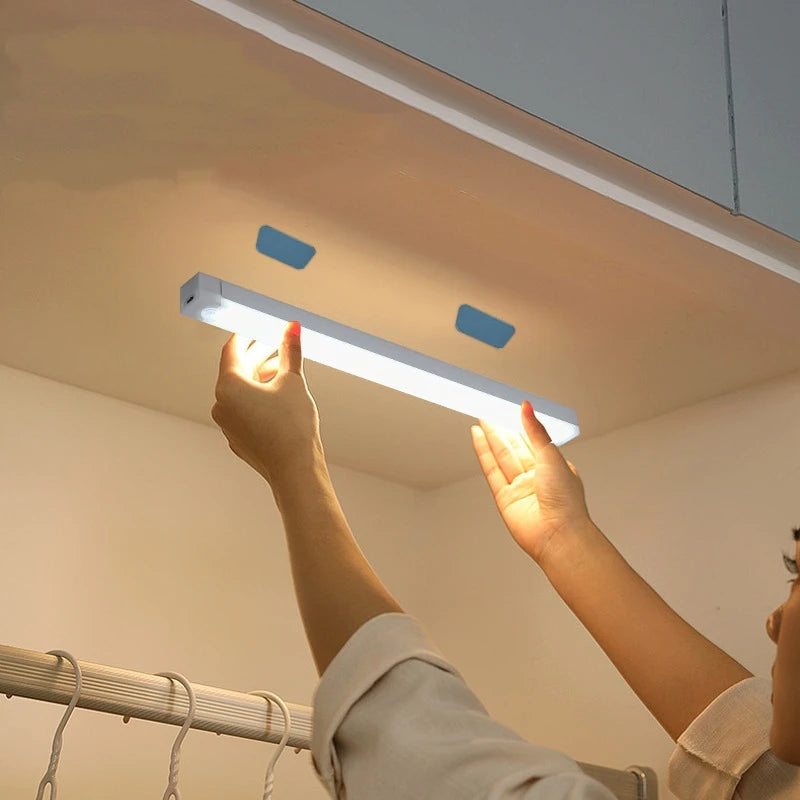 A hand is holding a white LED bar light with a magnetic mount, illuminating a room.