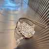 A light beige sequin accent chain shoulder bag with dangling pearl-like embellishments resting on a reflective surface.