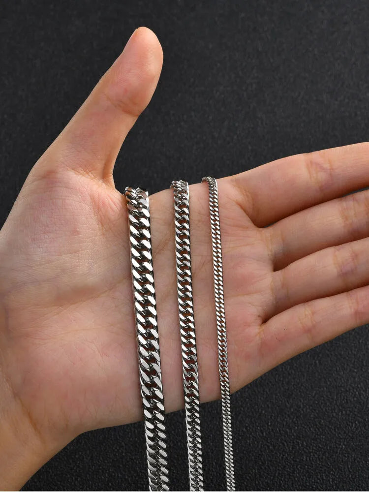 A hand holds several stainless steel Cuban link chains for display.