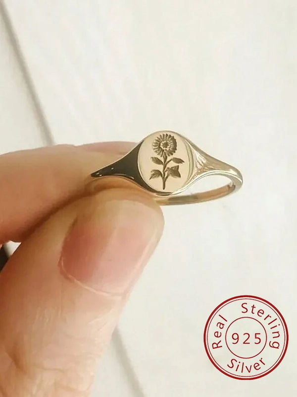 Gros plan d'une bague de fiançailles en argent sterling, fleur de tournesol personnalisée, tenue par une main.