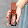 A hand holds a black stroller hook with a brown PU leather baby bag organizer attached.