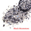 A pile of black moonstone crystal chips scattered on a white background.