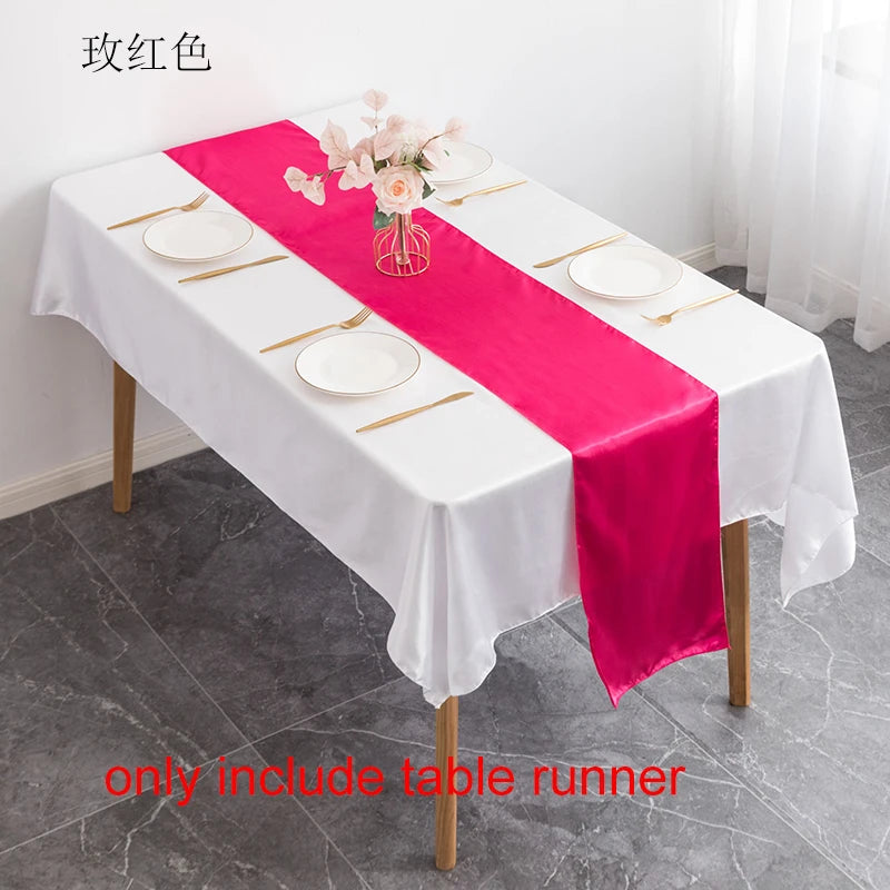 A pink satin table runner is displayed on a white tablecloth set for an elegant event.