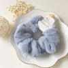 A light blue plush coil hair tie is displayed on a white plate next to a ball of natural twine.