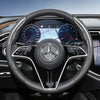 Close-up view of a black steering wheel with carbon fiber texture covers and a Mercedes-Benz logo.